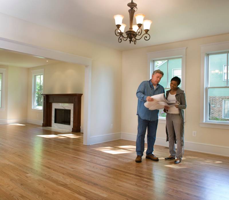 Couple inspecting a spacious, empty living room with hardwood floors and fireplace.