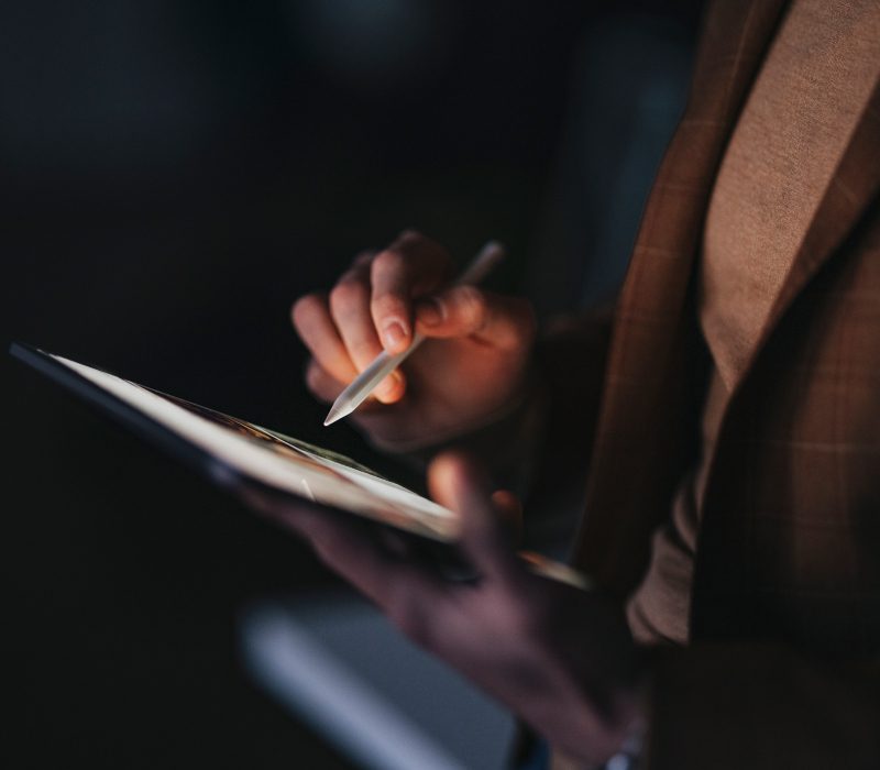 Person using a stylus to write on a tablet in low light.